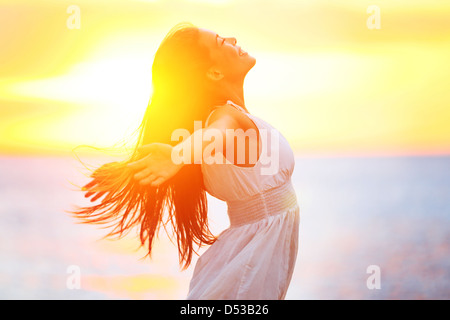 Side view of happy young mixed race woman in white dress with her arms outspread enjoying peace and serenity of golden sunet Stock Photo