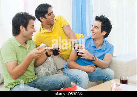Friends enjoying pizza with soft drinks and smiling at home Stock Photo