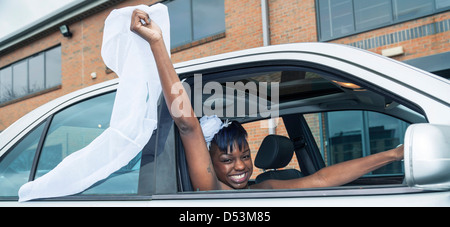 Bride driving off waving veil above car Stock Photo