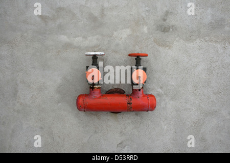 Red iron valve on a gray cement wall. Stock Photo