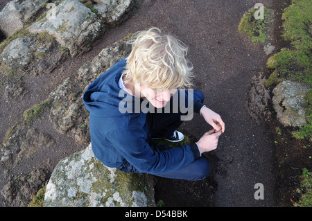 Young man aged 25 sitting on rock outdoors with blonde blond hair wearing blue Stock Photo