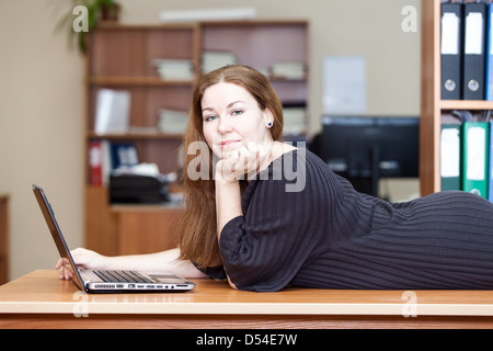 Happy joyful Caucasian woman laying on the desk with laptop in front Stock Photo