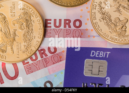 Solid gold coins contrasted with debit word on plastic card on euro note suggesting debt problems Stock Photo