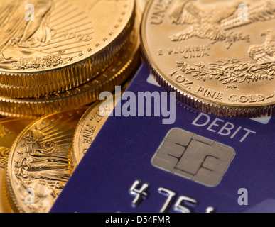 Solid gold coins contrasted with debit word on plastic credit card suggesting debt problems Stock Photo