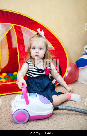 Happy small child playing with vacuum cleaner in domestic room Stock Photo