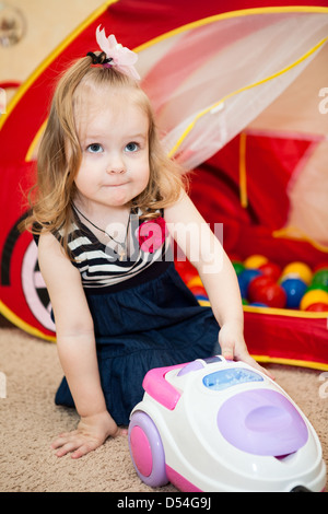 Cute young child playing with vacuum cleaner toy in domestic room Stock Photo