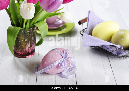 Pink, violet and white tulips in a glass vase with easter eggs on wooden background Stock Photo