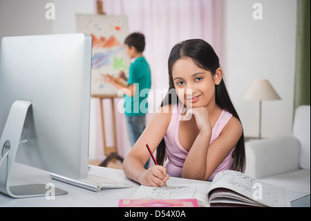 Girl studying at a study table with her brother painting on artists canvas Stock Photo