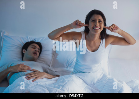 Man snoring with his wife covering ears with fingers on the bed Stock Photo