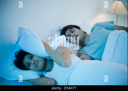 Man snoring with his wife covering ears with pillow on the bed Stock Photo