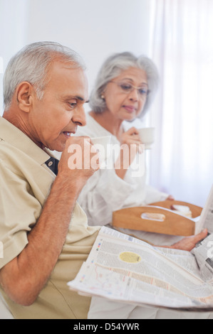 Senior couple having cup of tea with reading newspaper on the bed Stock Photo
