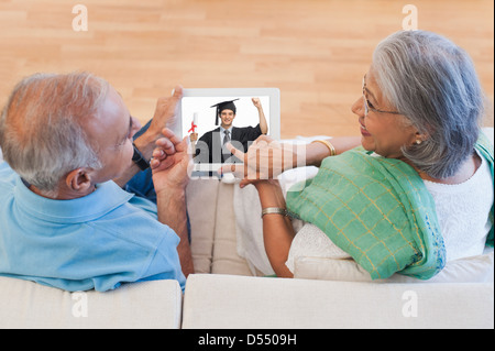 Senior couple pointing towards their graduate sons photograph and smiling Stock Photo