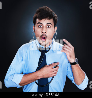 Close-up of a businessman listening to his heartbeat with stethoscope and looking surprised Stock Photo