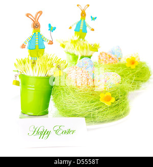 Beautiful colorful chicken eggs in the nest decorated with flowers and pretty rabbit toys isolated on white background Stock Photo