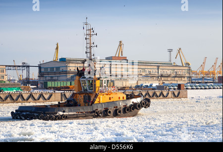 Small tug boat goes on icy channel in harbor of St.Petersburg cargo port Stock Photo