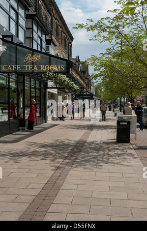 Independent retailers (eg Bettys Café Tea Rooms) are popular with shoppers visiting scenic town - sunny view of The Grove, Ilkley, West Yorkshire, UK. Stock Photo