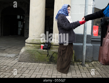 A young woman selling the Big Issue magazine to a customer paying money coins on the street in Crickhowell Wales UK   KATHY DEWITT Stock Photo