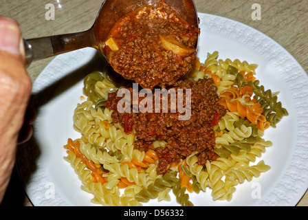 Ladle rich tomato mushroom meat Bolognese sauce over plate steaming hot cooked tricolour rotini pasta Stock Photo