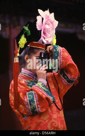 Young Chinese girl wears rented Qing Dynasty style wedding dress costume as she takes snapshots with a 35mm film pocket camera while visiting Tiantan Park in Beijing China Stock Photo