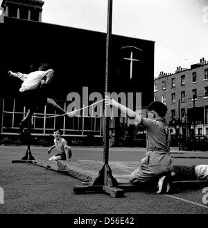 Historical 1950s.  School physical education. Young boy jumping over a rope onto a mat in the playground, London, England, UK. Stock Photo