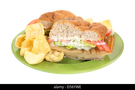 A bulky wheat roll turkey tofu sandwich with lettuce tomatoes and mayonnaise and chips on a green plate. Stock Photo