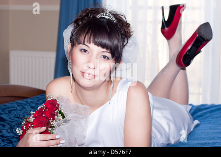 beautiful bride is rest on the wedding blue bed with bouquet of red roses Stock Photo