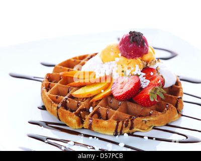 delicious home-made waffle with some slices of fresh peach and strawberries,fruit flavored ice cream and chocolate sauce Stock Photo