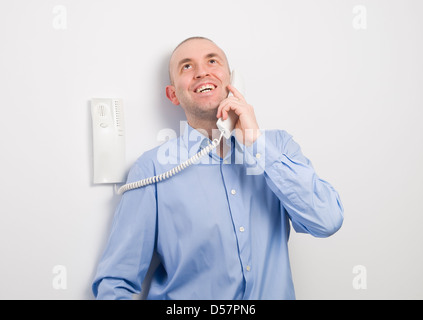 Man talking on a phone and smiling on white background. The man is wearing a blue shirt Stock Photo