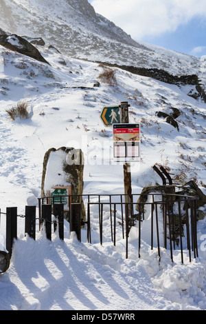 Deep snow drift around kissing gate and sign on footpath to Mount Tryfan north ridge in winter in Snowdonia, Ogwen Valley, Wales Stock Photo