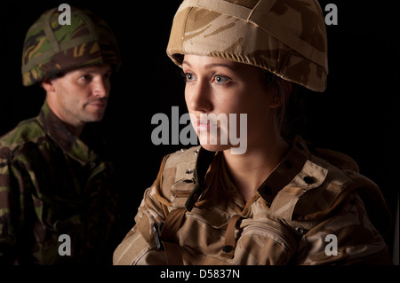 Female soldier in British Military desert uniform in foreground & male soldier in green camouflage uniform in the background. Stock Photo