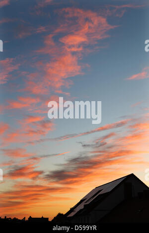 The clouds glow red over a house with solar collectors on its roof in Leipzig, Germany, 17 June 2010. A weather proverb says 'Red sky in the morning, shepherd's warning - red sky at night, shepherd's delight' ('Morgenrot - Schlechtwetter droht, Abendrot - Gutwetterbot'). Red sky at night can only occur when the setting sun in the west stands low and illuminates clouds farther east. Stock Photo