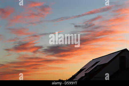 The clouds glow red over a house with solar collectors on its roof in Leipzig, Germany, 17 June 2010. A weather proverb says 'Red sky in the morning, shepherd's warning - red sky at night, shepherd's delight' ('Morgenrot - Schlechtwetter droht, Abendrot - Gutwetterbot'). Red sky at night can only occur when the setting sun in the west stands low and illuminates clouds farther east. Stock Photo