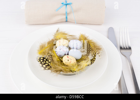 Easter table setting for a festive dinner - a decorative yellow nest with colourful ester eggs on a plate Stock Photo