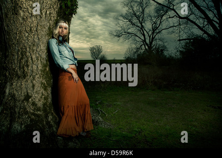 Blond woman leaning against tree in park or countryside Stock Photo