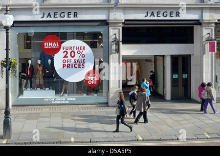 Shoppers walking on Regent Street pavement outside clothing store Jaeger retail business shop front window sale discount posters London England UK Stock Photo