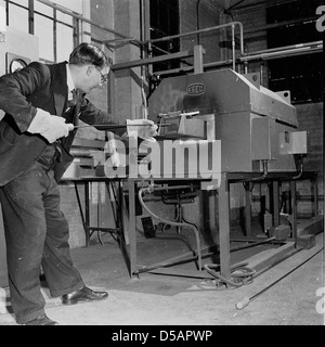 Historical 1950s. Industry.  An engineer wearing a suit and gloves checking the oil in a machine in a factory. Stock Photo