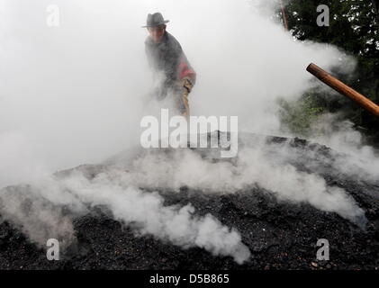 Jürgen Berger from the Black Forest processes a smoky charcoal pile in the Hotzenwald community Dachsber-Wolpadingen (district Waldshut), Germany, 5 August 2010. As like many years now, a charcoal pile is put together in the forest  for this summer and set on fire ceremoniously. On the 10 September, the pile shall be opened and the charcoal offered for sale. Photo: Rolf Haid Stock Photo