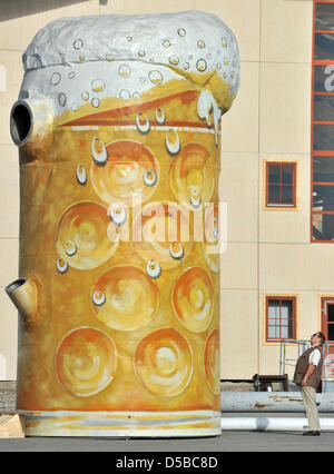 A man stands next to an oversized beer jug, that is supposed to be placed infront of a beer tent, on the area of the Oktoberfest in Munich (Upper Bavaria), Germany, 25 August 2010. The 177th Oktoberfest will take place between 18 August and 3 Oktober 2010 and with it, will celebrate its 200 year anniversary. The biggest folk festival in the world was initiated for the first time fo Stock Photo