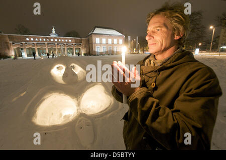 Canadian conceptional artist Steven van Vugt stands with a candle next to his ice sculpture before the Leipzig Grassi museum in Leipzig, Germany, 15 January 2010. The artist, who lives on Hornby Island (Canada), assembles sculptures exclusively from natural materials like driftwood, sea grass, snow and ice. During his visit in Leipzig, the masses of snow induced him to build ice an Stock Photo