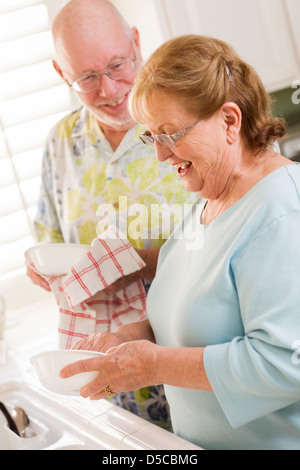Senior Adult Couple Having Fun Washing Dishes Together Inside Kitchen of Their House. Stock Photo
