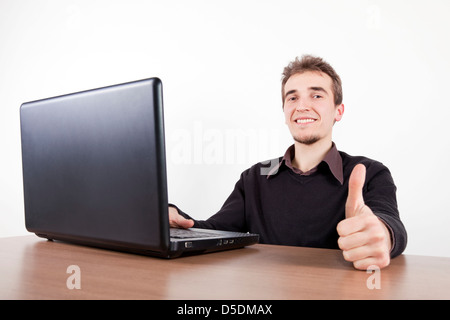 young man holding thumbs up with a laptop on a desk Stock Photo