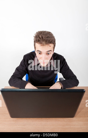 young man with laptop on a desk looking with huge eyes astonished at the screen Stock Photo