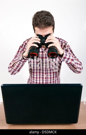 man looking at a laptop with binoculars Stock Photo