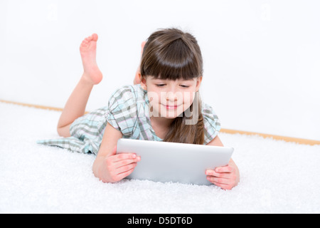 Young girl (6-7 year) looking and playing with digital tablet in a white room.
