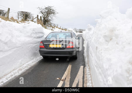 Carrickfergus, Northern Ireland. 29th March, 2013. A car drives between deep walls of snow which line a recently cleared rural road Stock Photo