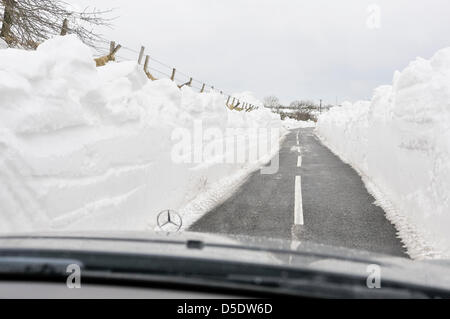 Carrickfergus, Northern Ireland. 29th March, 2013. A Mercedes car drives between deep walls of snow which line a recently cleared rural road Stock Photo