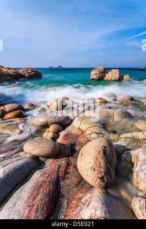 Boulders on Porth Nanven cove with Bubble Gum Rock and The Brisons in the distance. Stock Photo