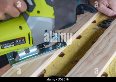 Close-up of a man using a jigsaw on a piece of wood. The jigsaw is carving out semi-circles to make a wine rack. Stock Photo