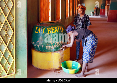 two woman drink holy water from a barrel upon the entrance door of the catholic cathedral in Bobo-Dioulasso, Burkina Faso Stock Photo