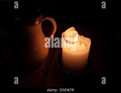 Burning candle and clay cup of beer on table in old restaurant Stock Photo